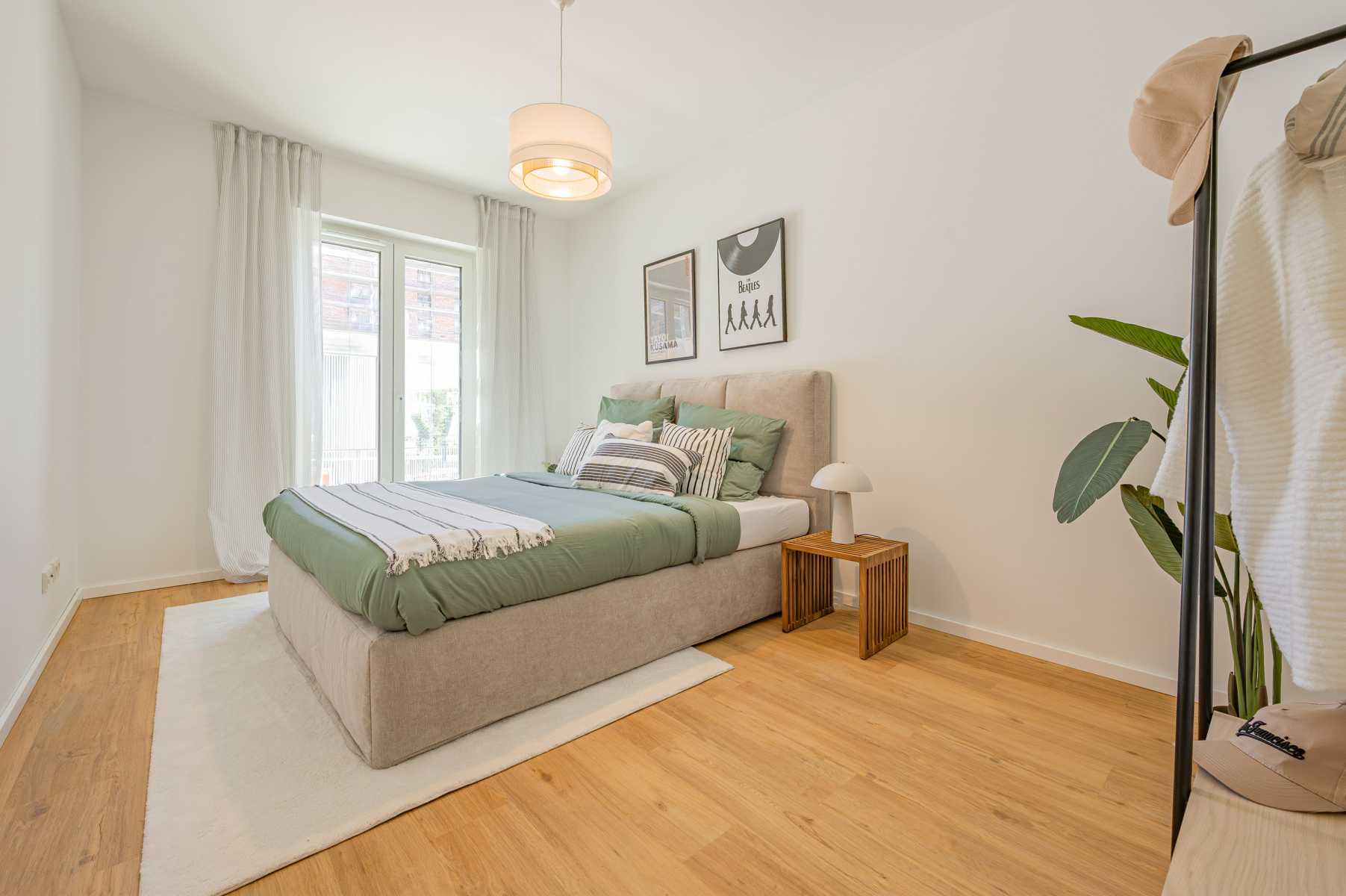 Helles Schlafzimmer mit Doppelbett, Holzboden, Dekopflanze und großen Fenstern.