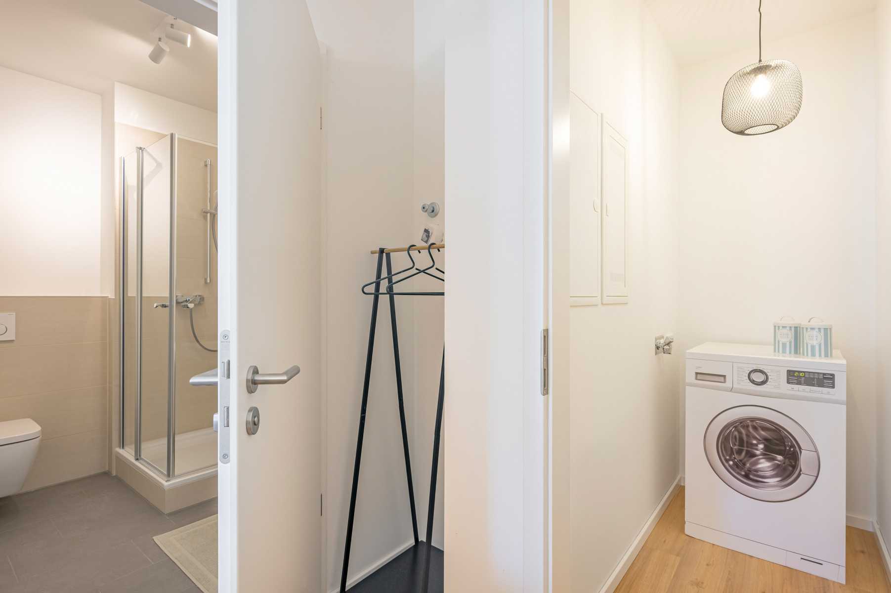 Badezimmer mit Dusche und Toilette, daneben ein Raum mit Waschmaschine.