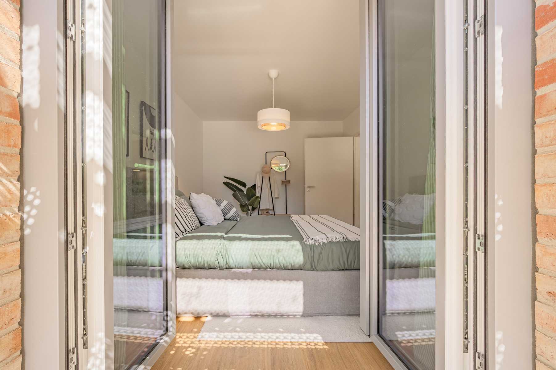 Helles Schlafzimmer mit Doppelbett, Blick durch geöffnete Glastüren.