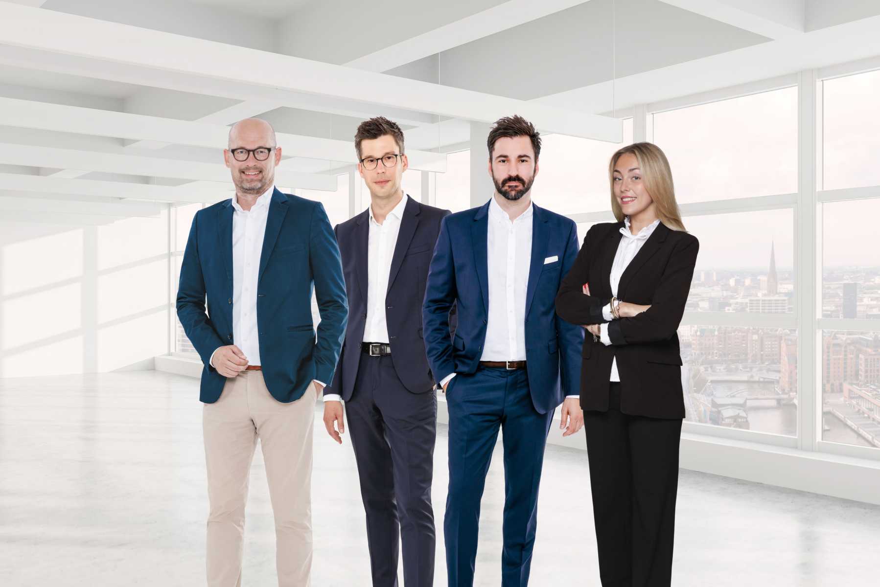 Vier Personen im Business-Outfit stehen in einem hellen, modernen Büro.