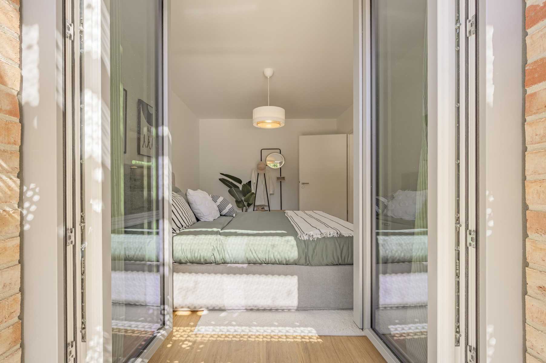 Helles Schlafzimmer mit Doppelbett, grüner Bettdecke und offener Terrassentür.