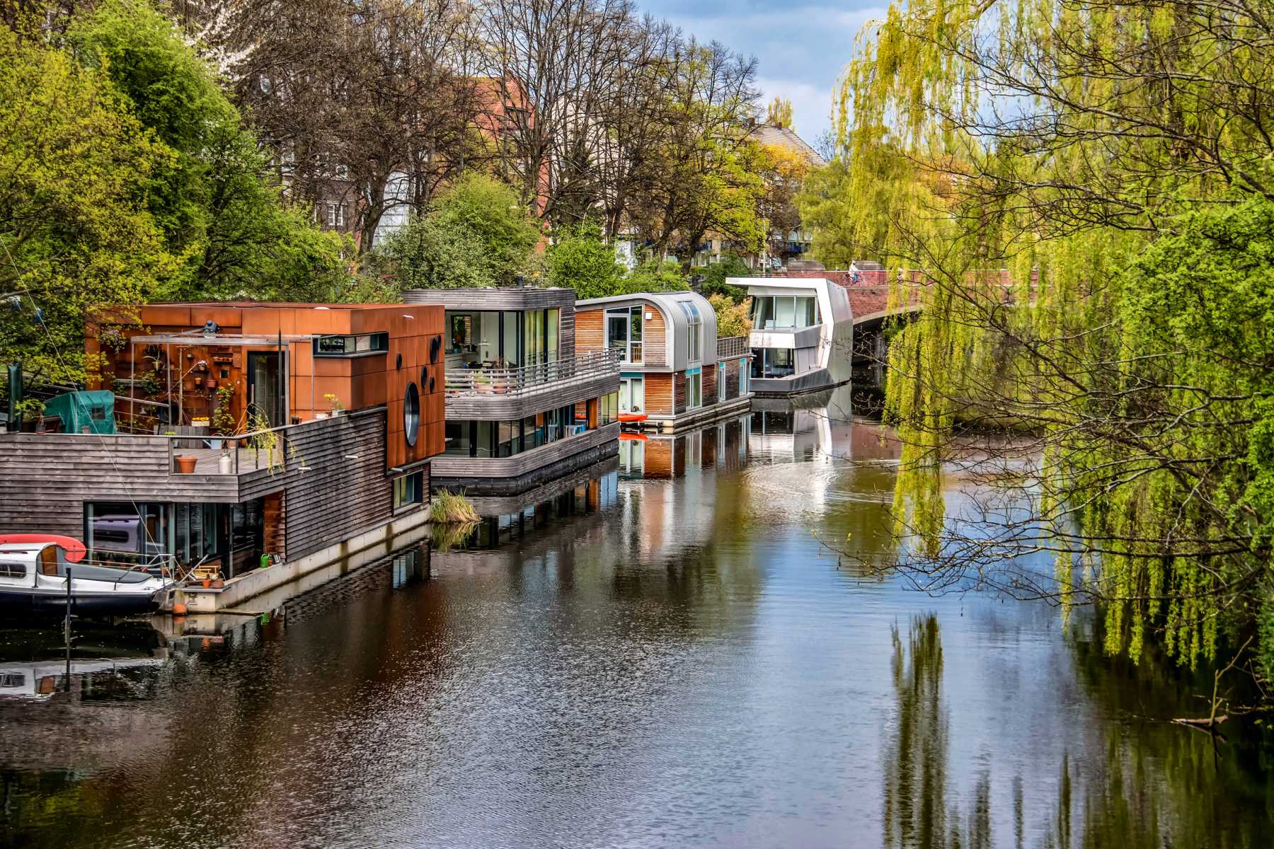 Moderne Hausboote liegen an einem ruhigen Fluss, umgeben von viel Grün.